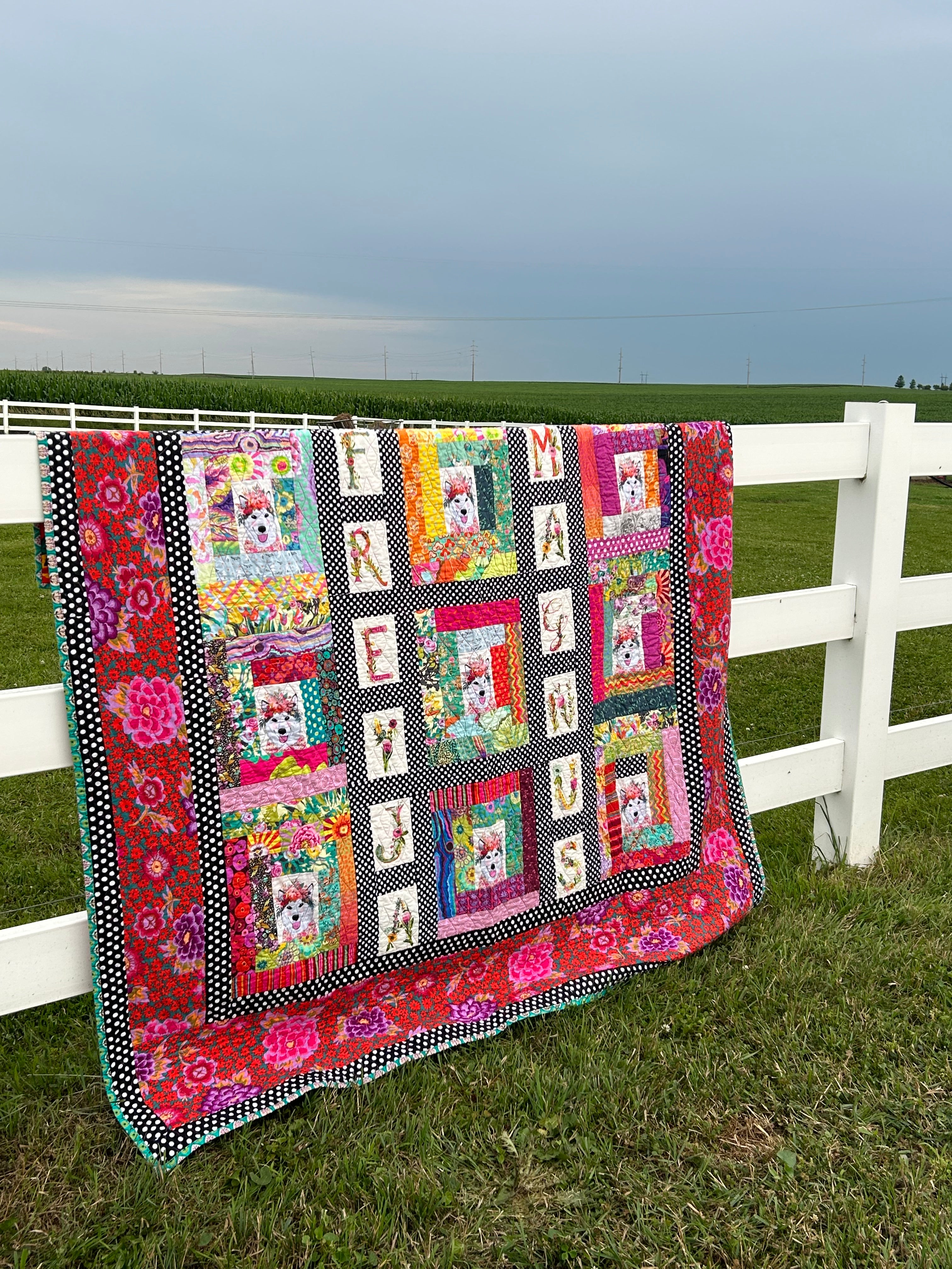 Colorful quilt on a white fence against a grassy background