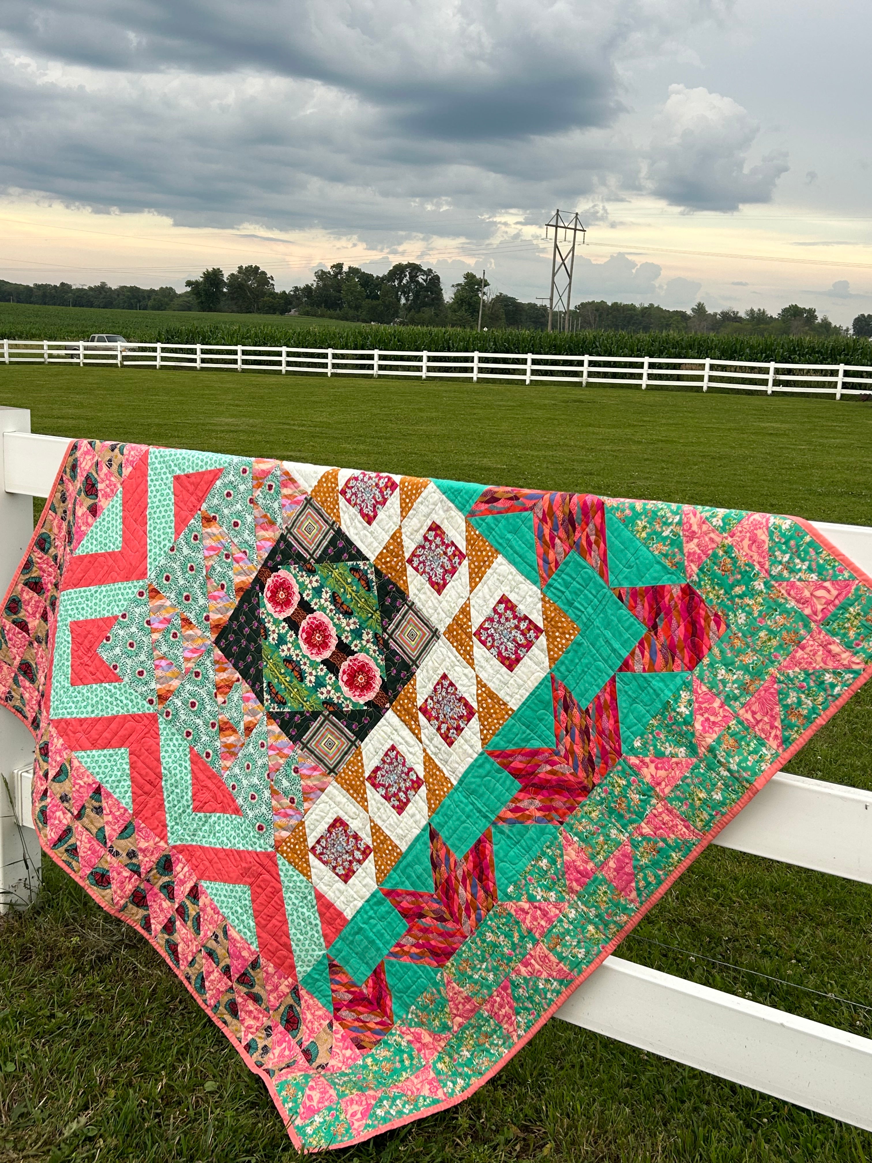 Colorful quilt with geometric patterns on a white fence by a field